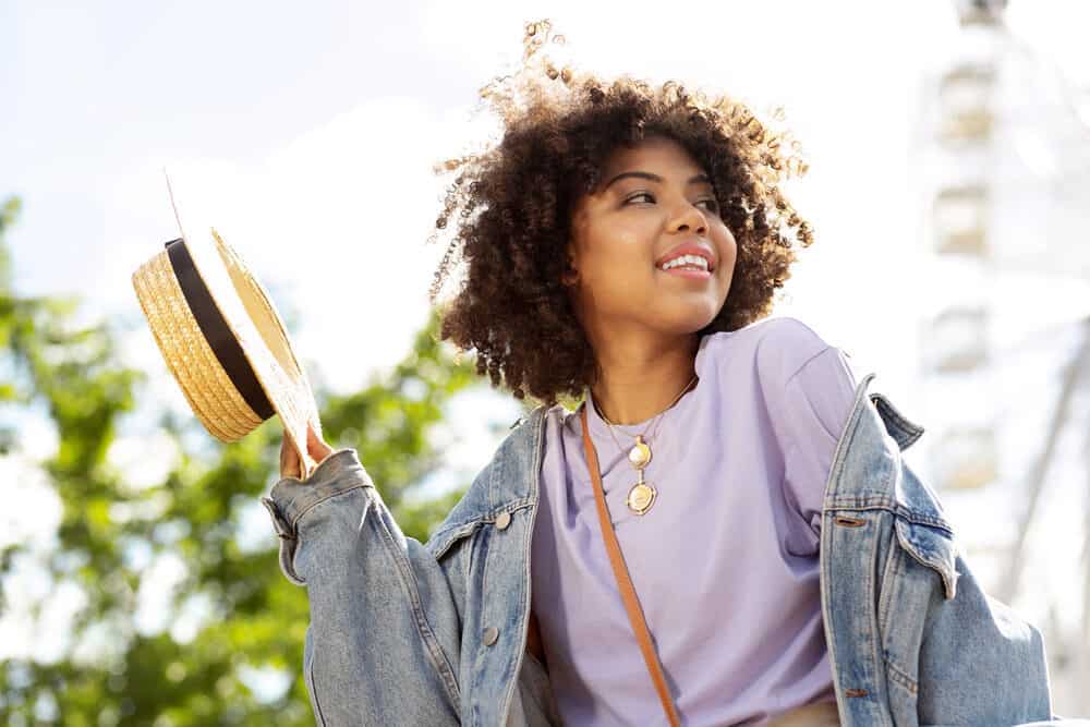 A curly young girl is removing her straw hat.