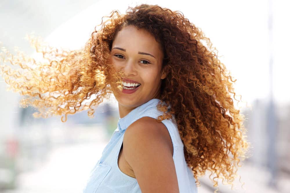 Young woman with naturally curly hair styled with red dye and toned with a purple shampoo