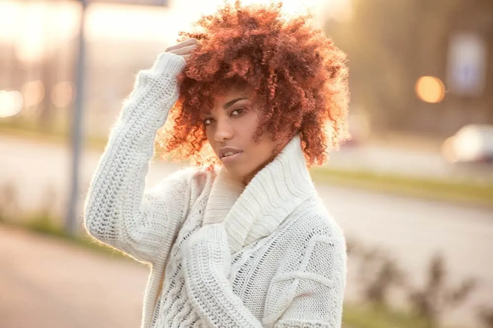 Black lady with bouncy curls colored with semi-permanent color wearing a white sweater.
