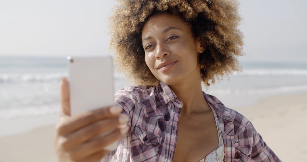 Woman taking an iPhone selfie with blonde hair dye on naturally dark brown coils.