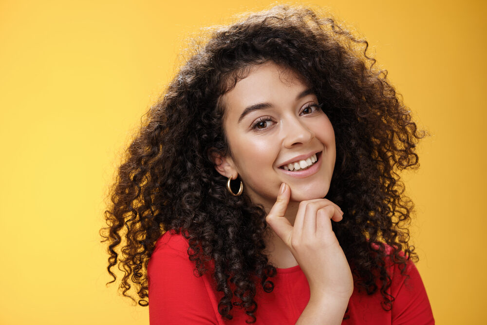 A cute white lady wearing a red shirt with curly permed hair curled with perm rods to alter her natural texture.