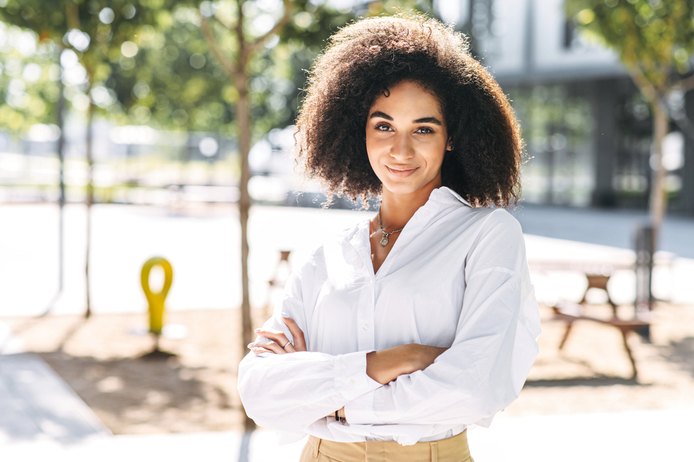 Confident African American with healthy hair standing outside with her arms folded.