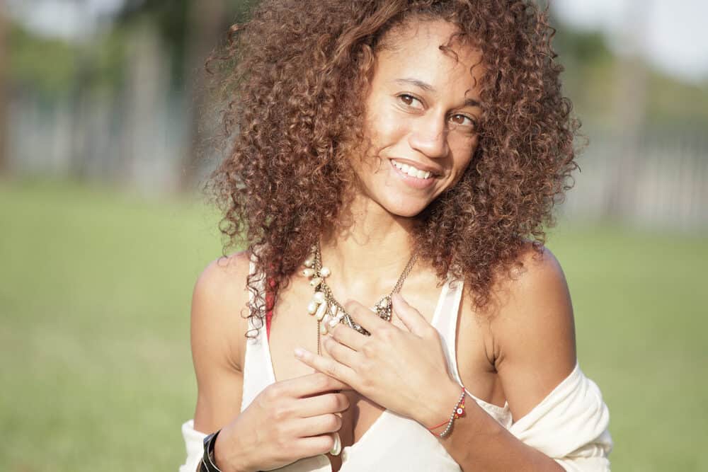 Sun-kissed black female with curly hair follicles and an oily scalp standing outside.