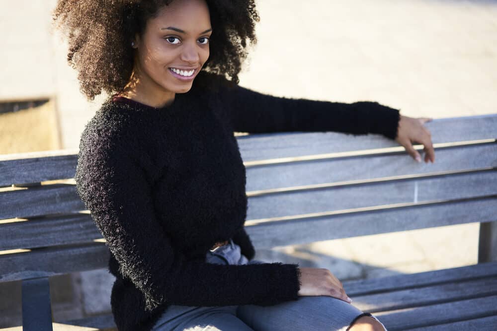 Optimistic African American woman with healthy hair sitting on a bench at the park.