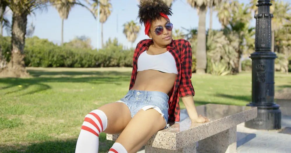 Why Does My Hair Take So Long To Dry? Naturally? After Bleaching? 2 Attractive African American woman with 4A curls wearing a checkered shirt while sitting on a park bench.