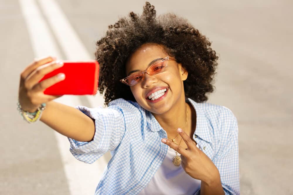 Beautiful young black girl with dark brown hair soaking up the sun's rays while taking a selfie.