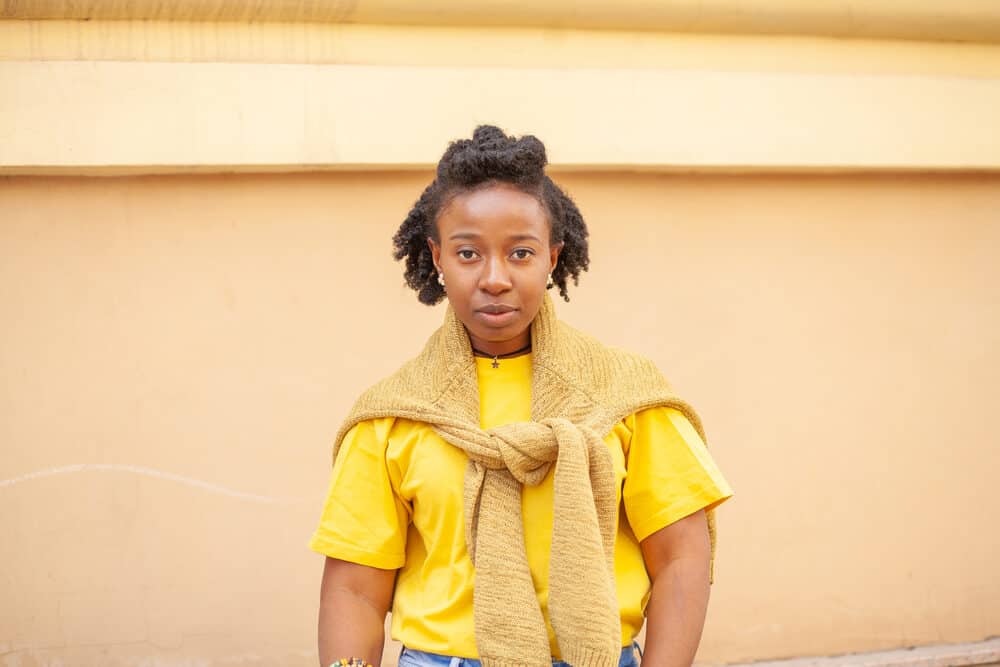 Black girl with dry hair properly dried to avoid a musty smell wearing a yellow t-shirt and sweater tied around her arms.