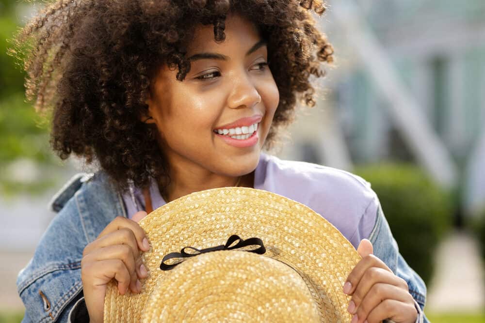 Joyful female with curly hair wearing a hat to cover up drug-induced hair loss caused by blood pressure meds.