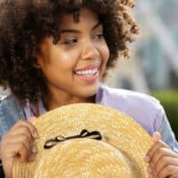 Joyful female with curly hair wearing a hat to cover up drug-induced hair loss caused by blood pressure meds.