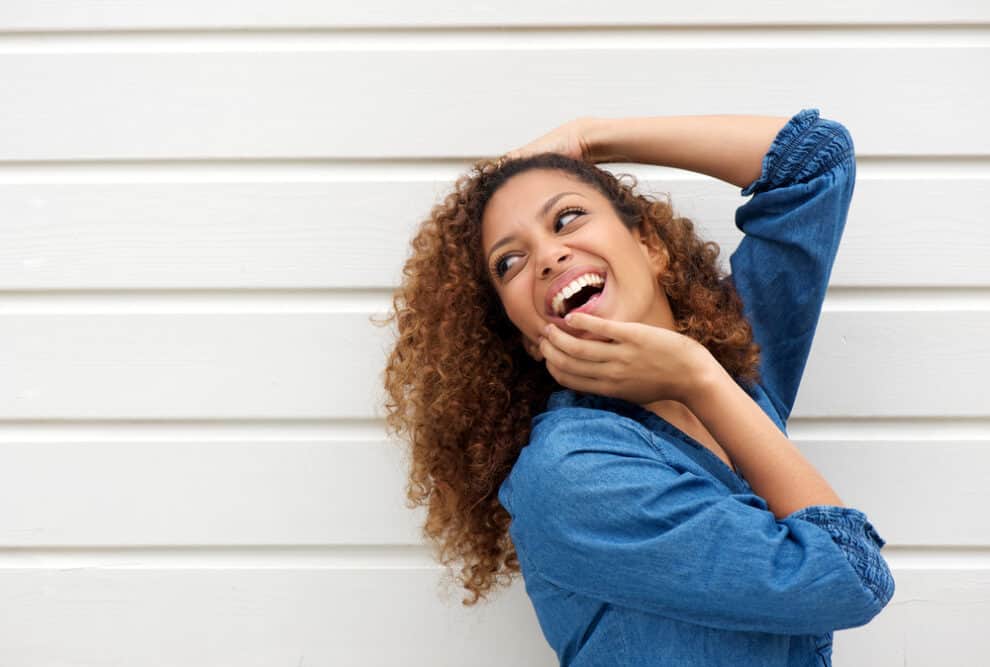 Black girl with a balayage curly hairstyle with her roots untouched while her natural shades show underneath.