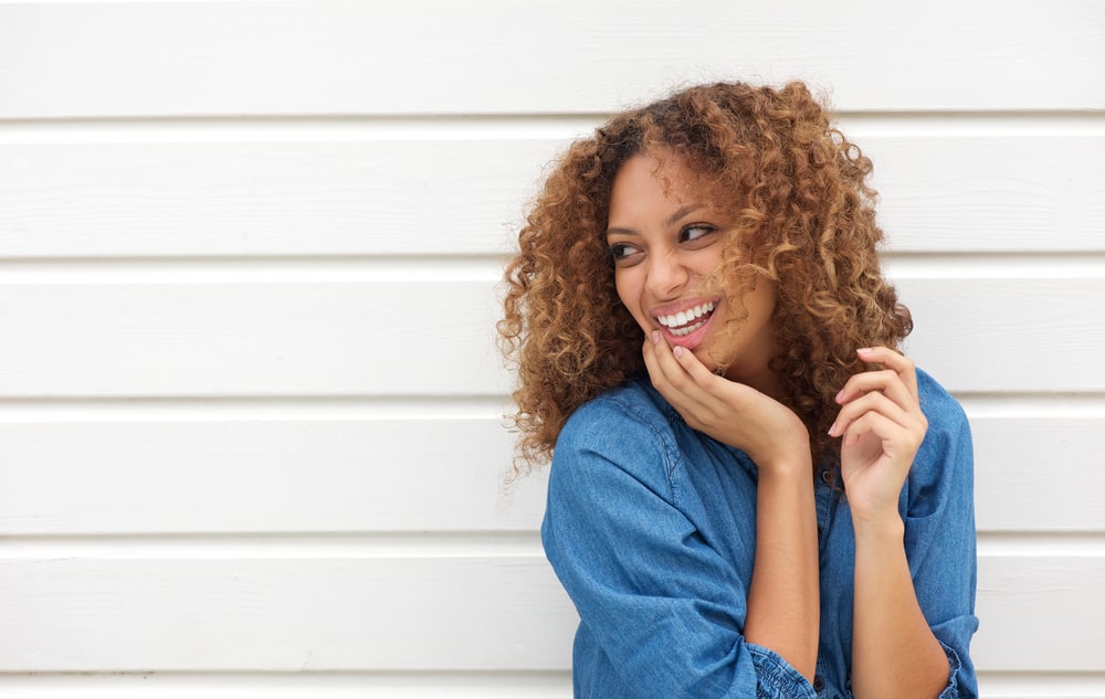 Black girl with dark-colored roots with caramel skin creating a sharp contrast between her hair and skin.