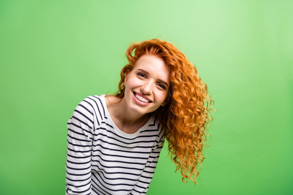 Lady with naturally curly hair wearing a winter sweater while smiling.