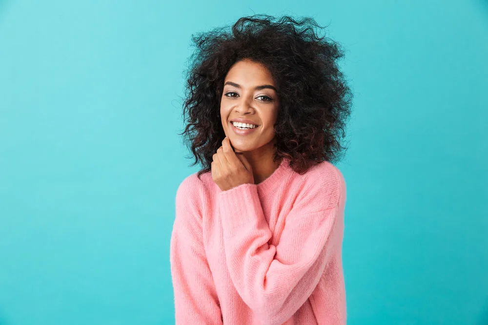A beautiful black woman with dark brown color-treated hair wearing a pink sweater.