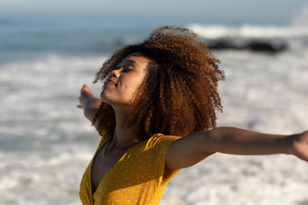 Cute African American female with natural lashes wearing a water-resistant lace wig while enjoying the beach.