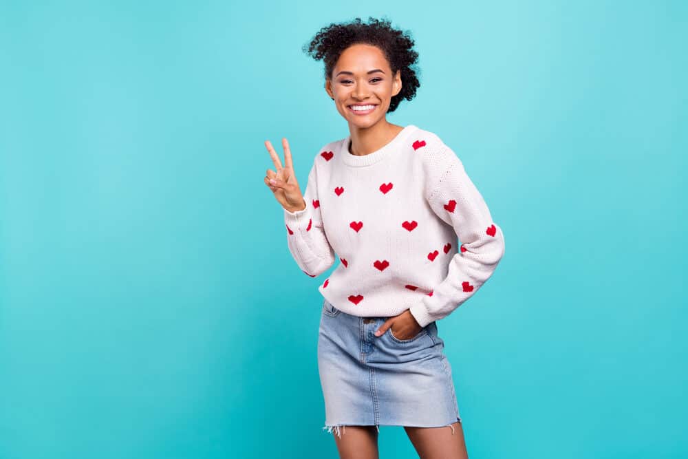 Cute black girl wearing a casual outfit with pastel colours while making a peace sign with her fingers.