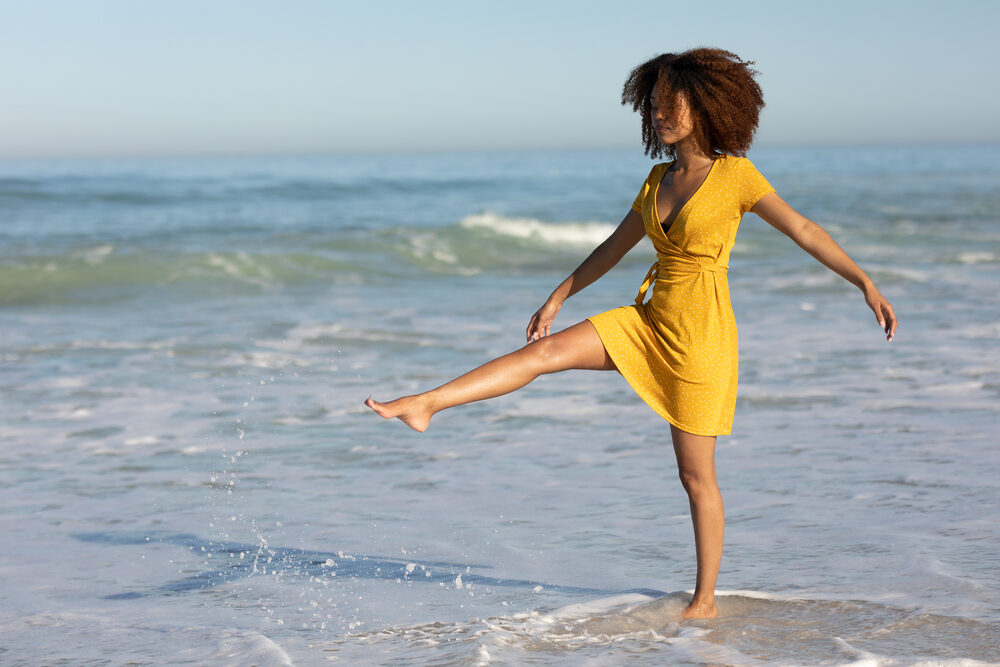 Black female wearing a yellow dress and fake eyelashes while enjoying the beach water.