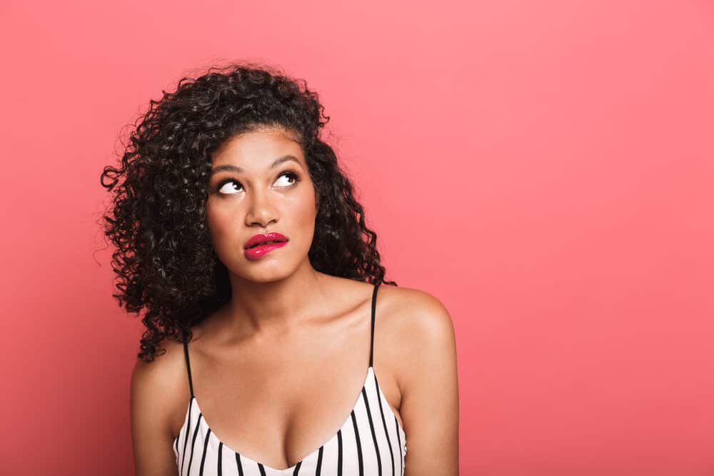 African American woman loose curls on thin hair wearing a black and white casual top with red lipstick.