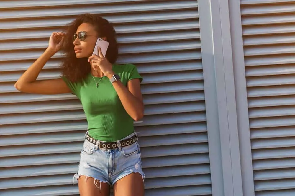 Black lady with a 4B natural curl pattern wearing a green shirt, black belt, and cut-off jeans shorts.