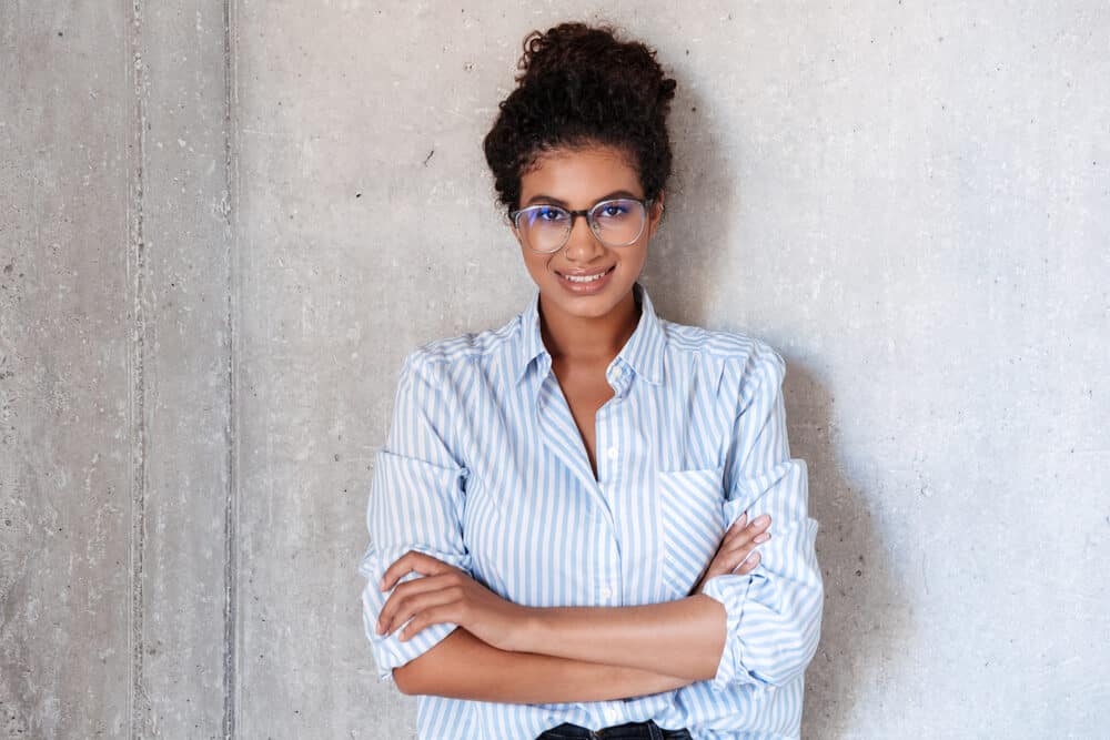 A beautiful lady wearing a blue and white dress shirt and glasses with colored hair from a professional colorist.