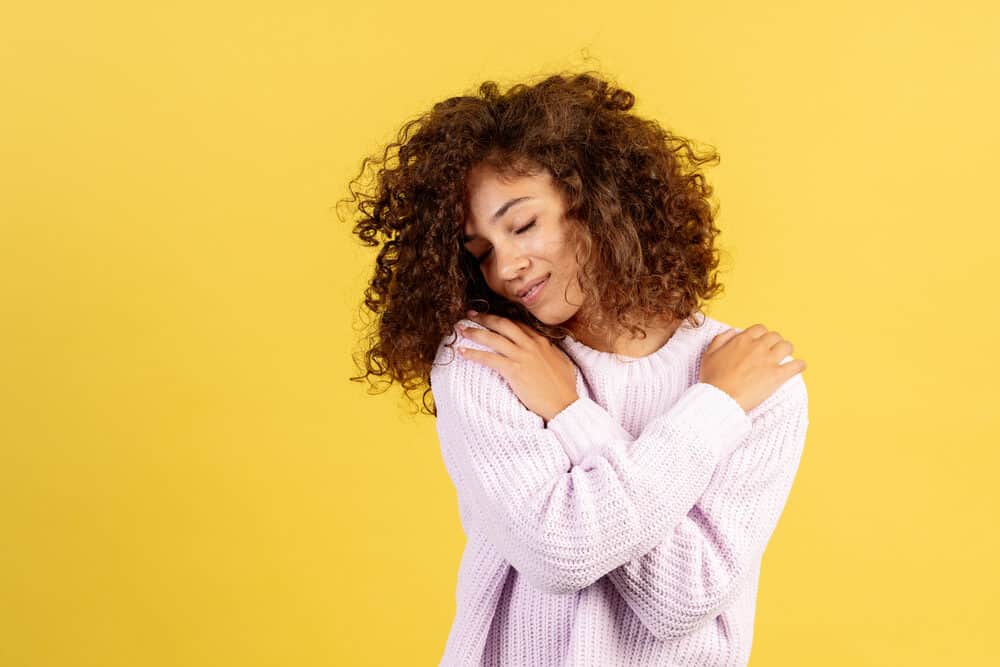 Lovely African American girl with moisturizing cream on her face and hands wearing a light pink sweater.