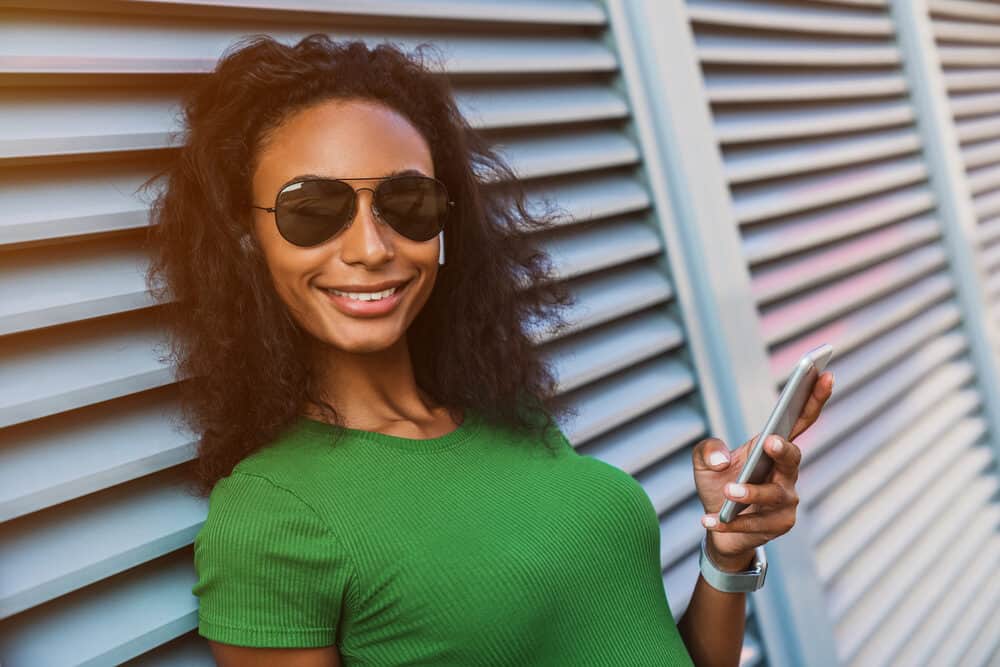 Beautiful African American female with curly natural hair wearing straight hair while using her iPhone.