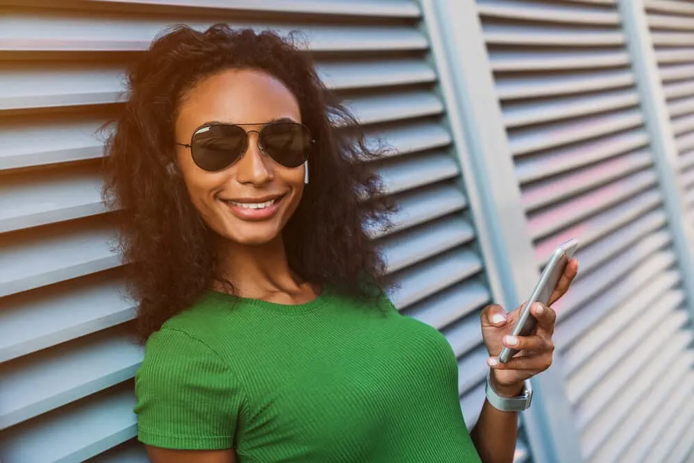 Does Straightening Curly Hair Damage It? Ruin It Forever? 1 Beautiful African American female with curly natural hair wearing straight hair while using her iPhone.