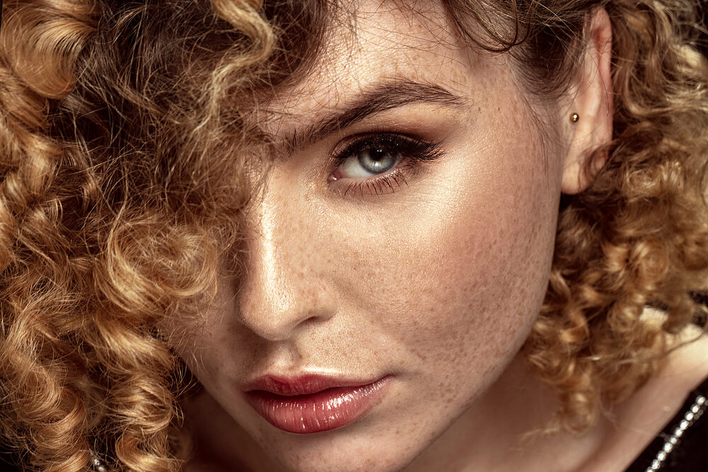 Cute Caucasian female with naturally curly hair and reddish-brown freckles.