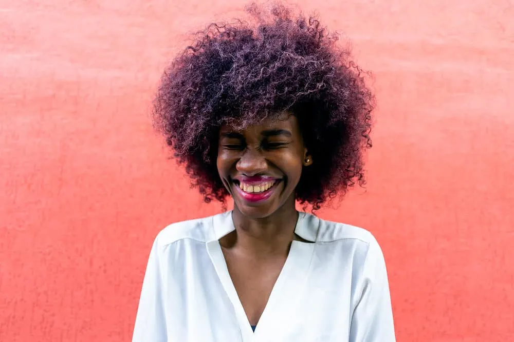 Is It Better to Dye Clean or Dirty Hair To Get the Best Results? 5 Female with 4B curl with dark brown and purple hair colors wearing red lipstick and white dress shirt.