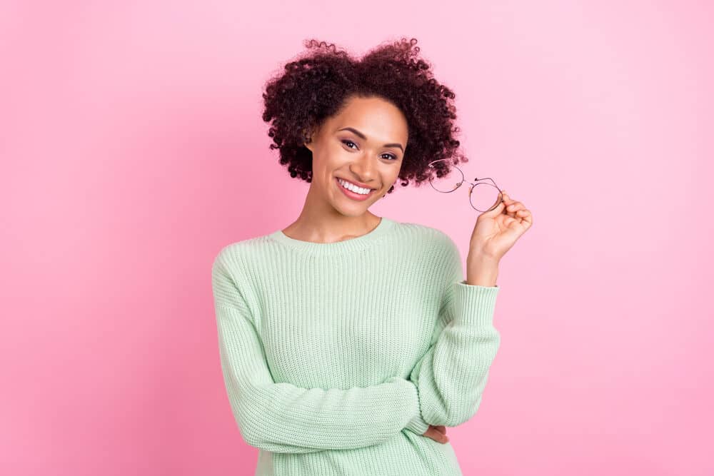 Lady with a strawberry natural shade on 3B curls wearing round glasses and pink lipstick.