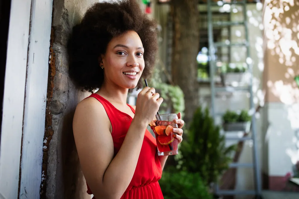 Stylish black female drinking a healthy beverage with biotin to promote healthy hair growth.