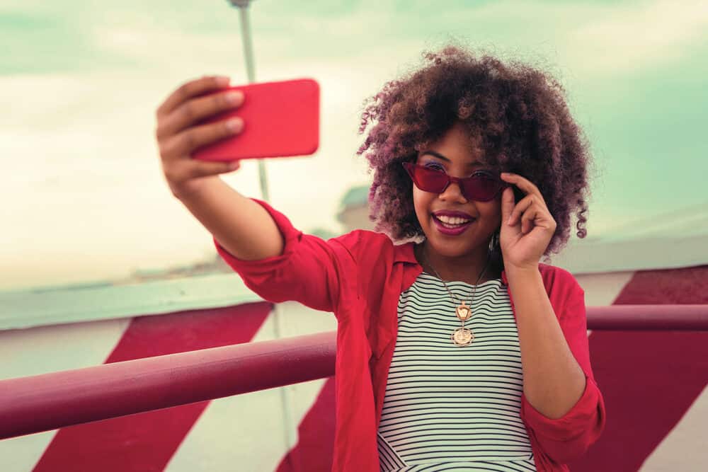 A cheerful African American woman with color-treated hair takes a selfie after using color-safe shampoo.