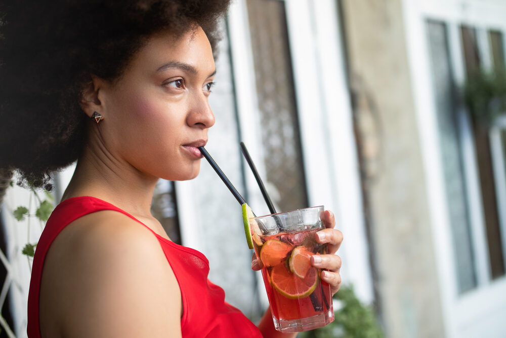 Beautiful afro woman with thicker hair fibers drinking a flavored sweet tea with lime chunks.
