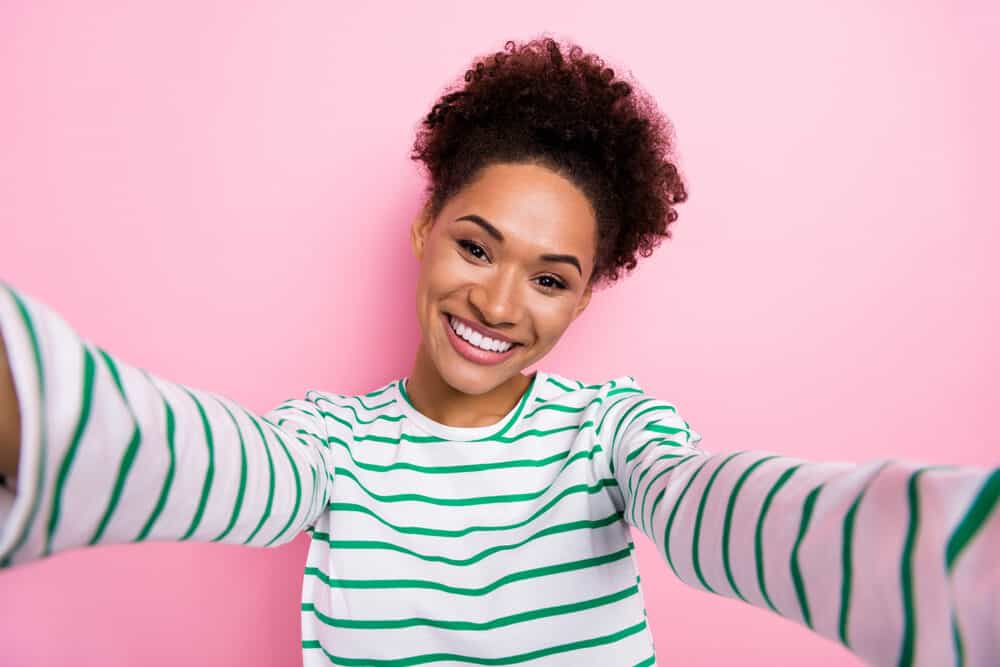 Cute black lady with a dark brown natural hair color with curly hair strands wearing a green and white shirt.