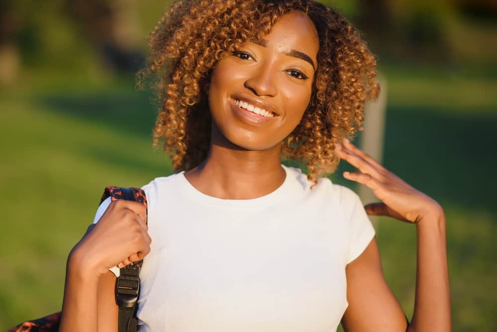 African American female wearing a white t-shirt with light brown dyed hair on naturally black hair.