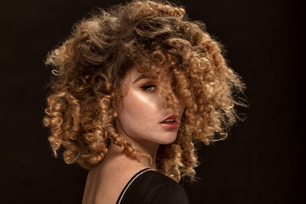 A white lady with fragile hair following chemical services wearing defined curls and red lipsticks.