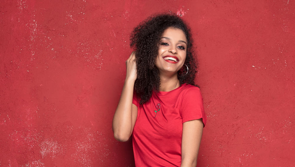 Lady with 3B hair keeping her curls smooth by brushing hair with her fingers and a detangling brush.