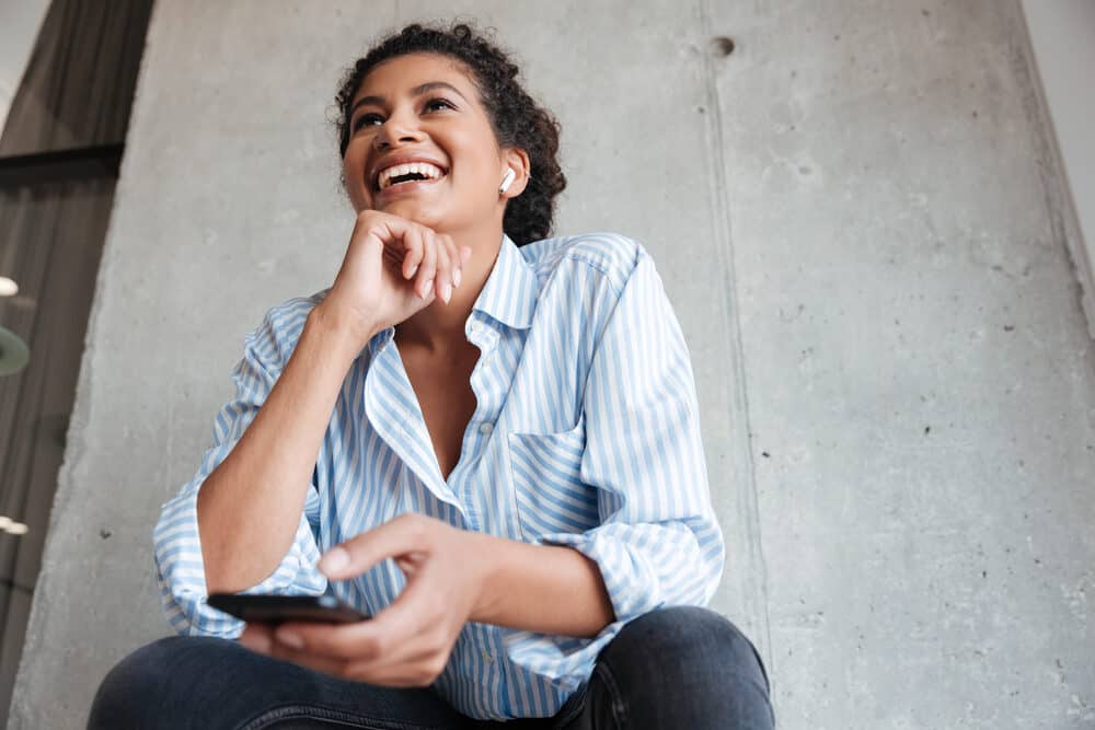 An attractive black woman sitting outside using a cell phone with a dark brown natural colour.