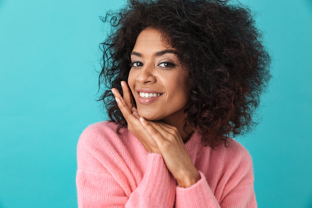 A black lady with thin hair strands on a dark brown natural color wearing a pink wool sweater.