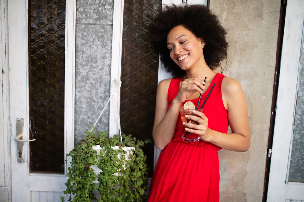Black woman with healthy hair growth on 4B curls wearing a red dress while drinking raspberry tea.