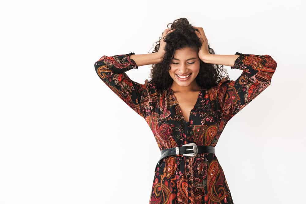 Excited young lady with 3B curls laughing and smiling while holding her hands on her head.