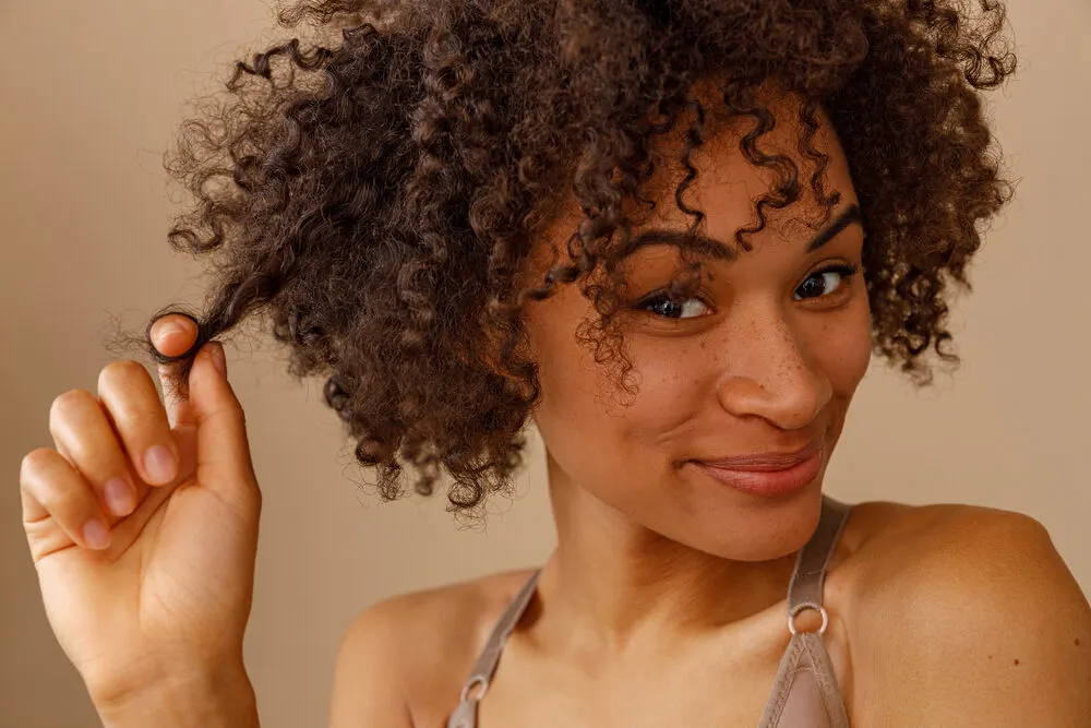 Black woman with fine hair touching her 3C natural curls styled with hair styling powder.