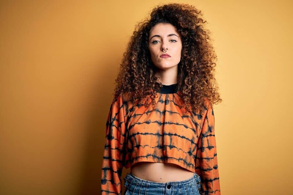 A white woman wearing an orange and black shirt with light density Malaysian hair.