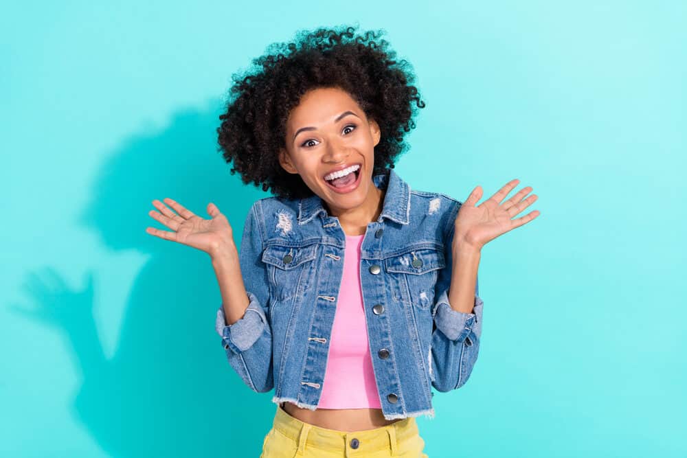 Black girl with a light skin tone wearing a pink shirt, yellow pants, and a torn blue jean jacket.