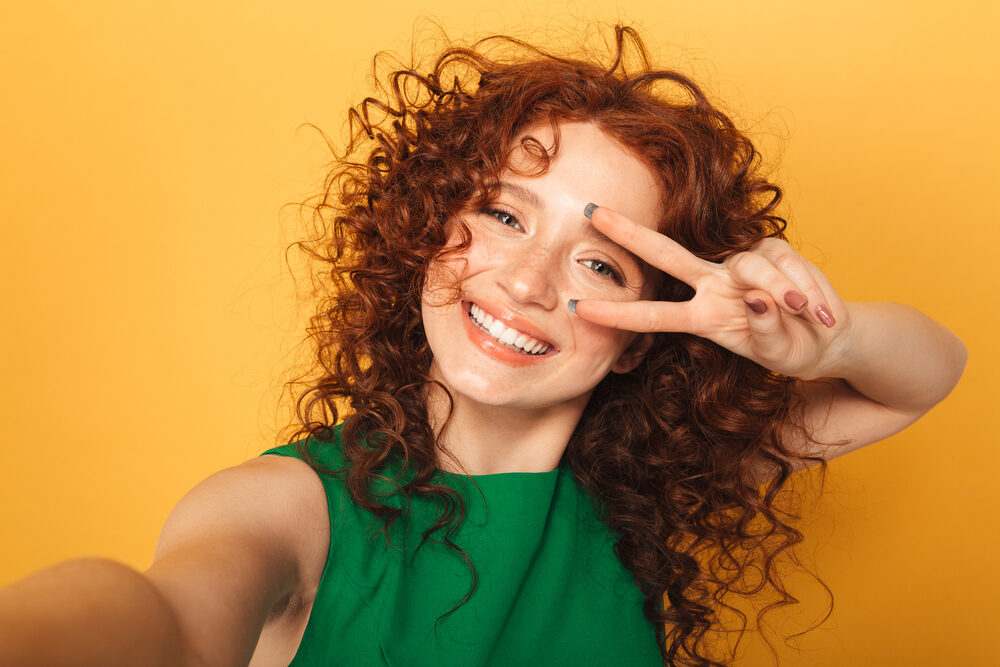 A funny redhead woman showing a peace sign after getting perm and bleach chemical treatments on 1C hair type.