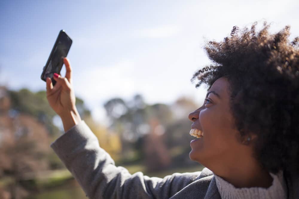 Beautiful woman with 4A natural curls styled with expeller-pressed coconut oil taking selfie in the park.