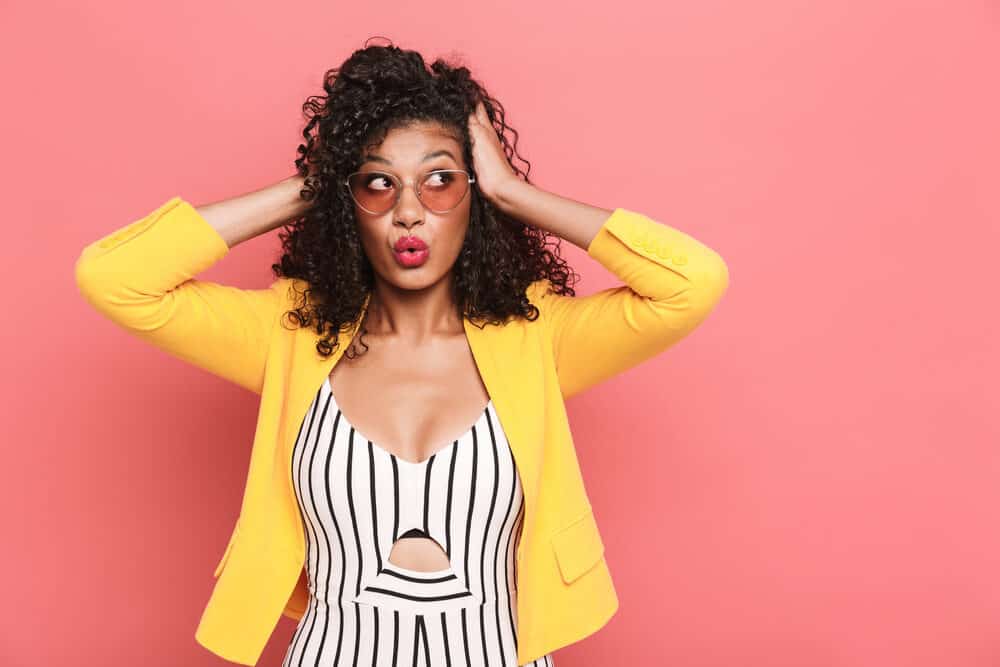 Excited young black girl with frizzy hair wearing a wash and go hairstyle with rose-colored glasses.