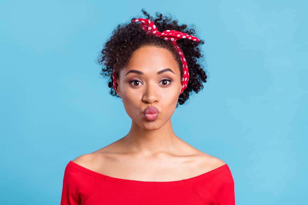 A black female with frizzy hair wearing red lipstick with freckles on her nose making a duck face.