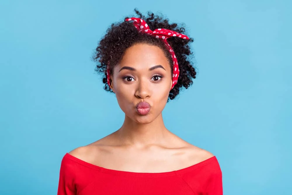 A black female with frizzy hair wearing red lipstick with freckles on her nose making a duck face.