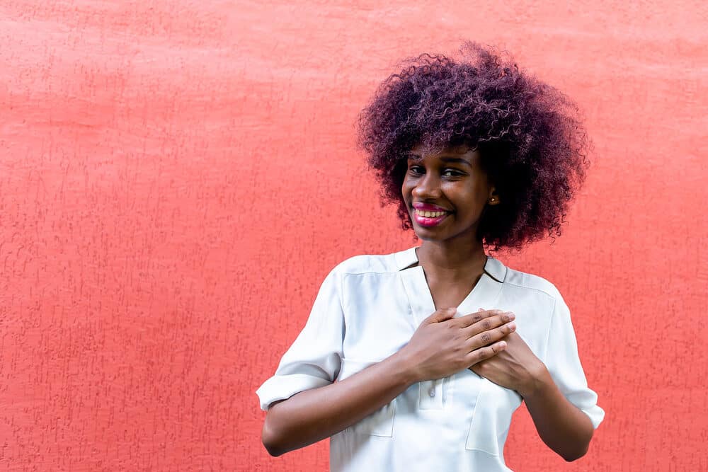 An African American woman with freshly washed hair covers her heart following a salon appointment.