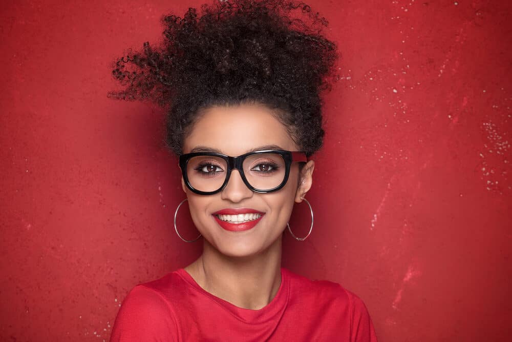 African American with a 3C curl pattern wearing red and black glasses with hoop earrings and red lipstick.